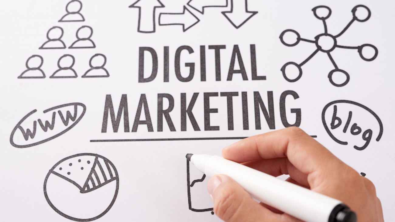 From above shot of crop hand using marker pen to draw icons near digital marketing writing on paper sheet